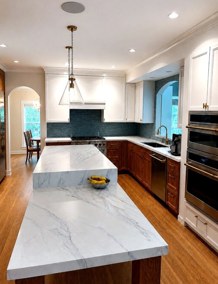 Custom kitchen with a long stone island, mixed wood and white cabinetry, and pendant lights.
