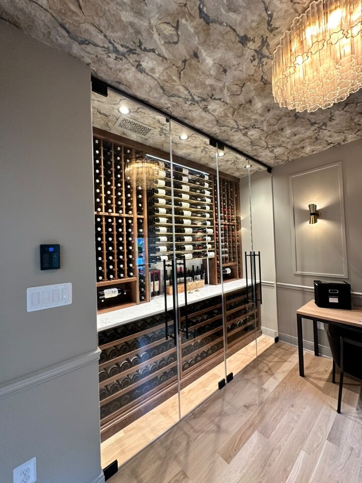 Glass-front wine storage with illuminated racks, a chandelier, and a patterned ceiling.