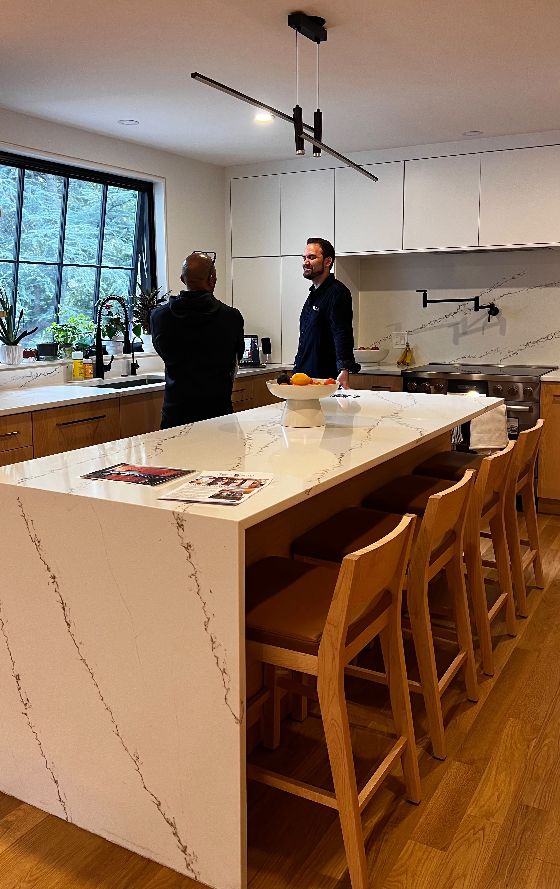 Visitors discussing the kitchen beside its stone island and wood cabinetry.